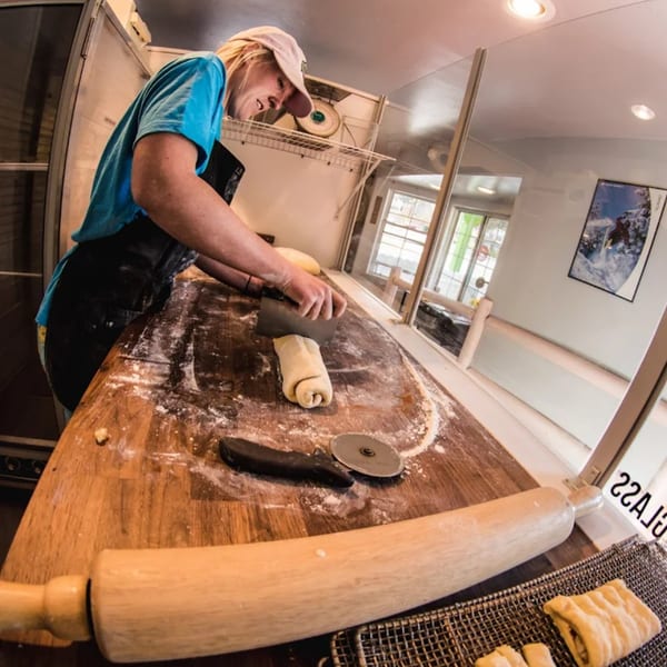A Dank Donuts baker in an apron smiles while cutting dough on a floured wooden table.