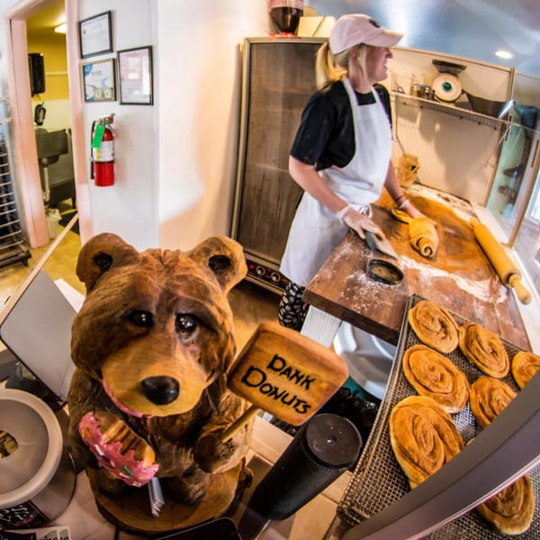 A baker prepares Dank Donuts pastries on a flour-dusted wooden table, next to a bear statue.