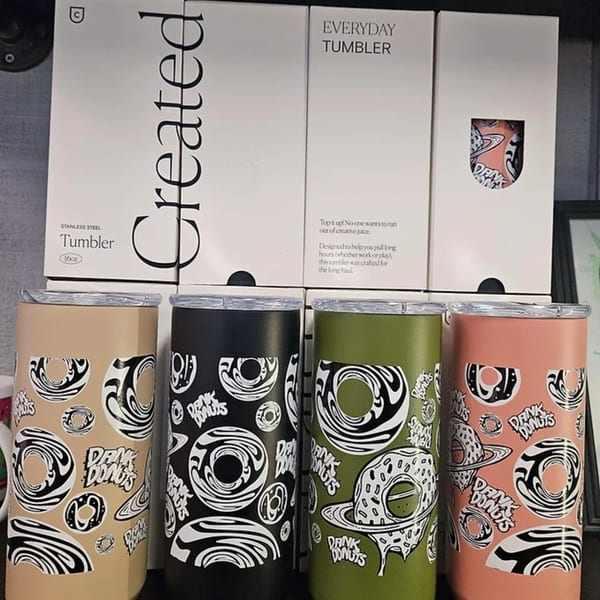 Four Dank Donuts tumblers in beige, black, green, and pink with donut designs and packaging.