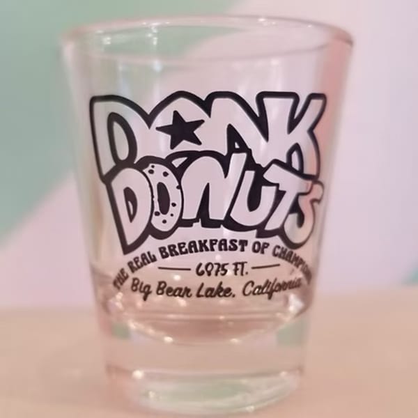 A clear shot glass with the Dank Donuts logo and "The Real Breakfast of Champions" text.