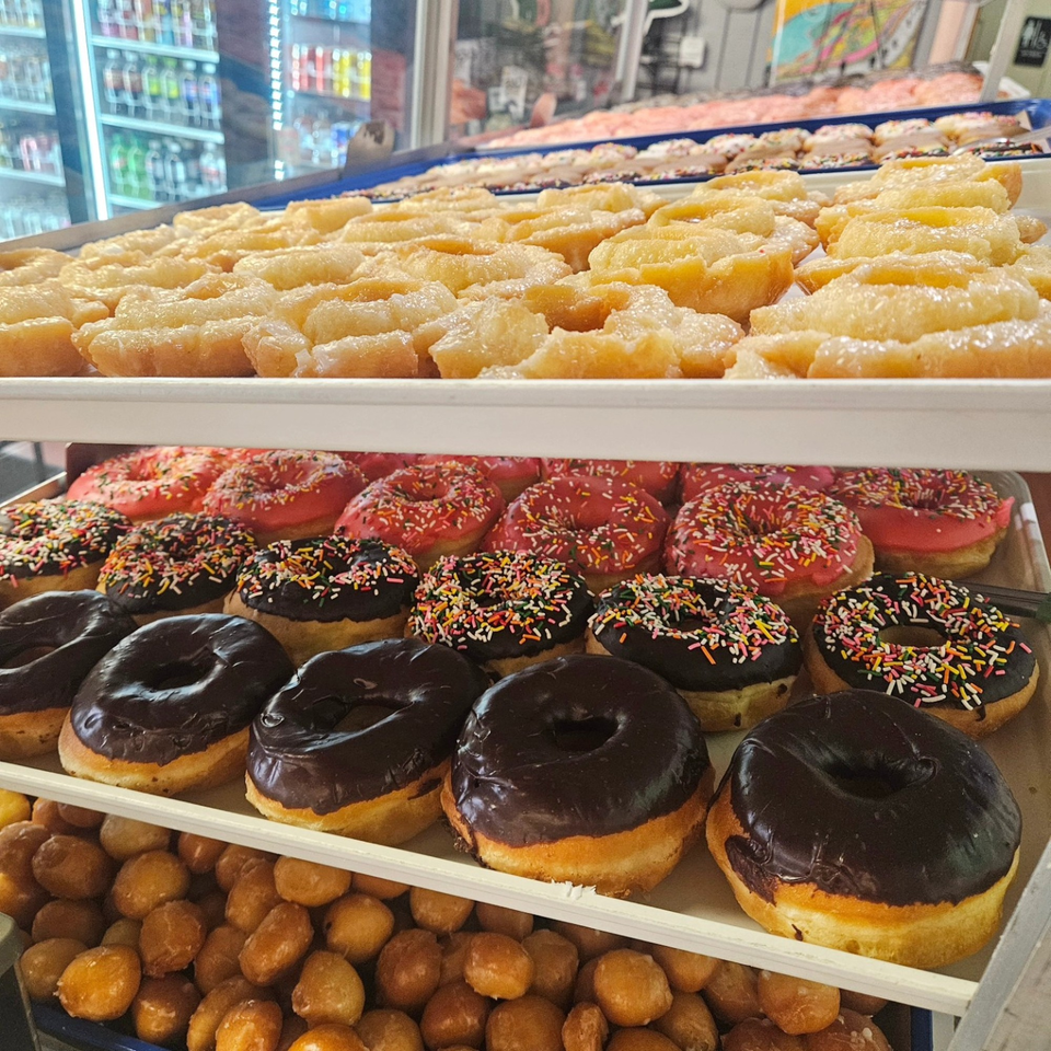 A display case filled with various Dank Donuts, including glazed, chocolate, and sprinkle-covered varieties.