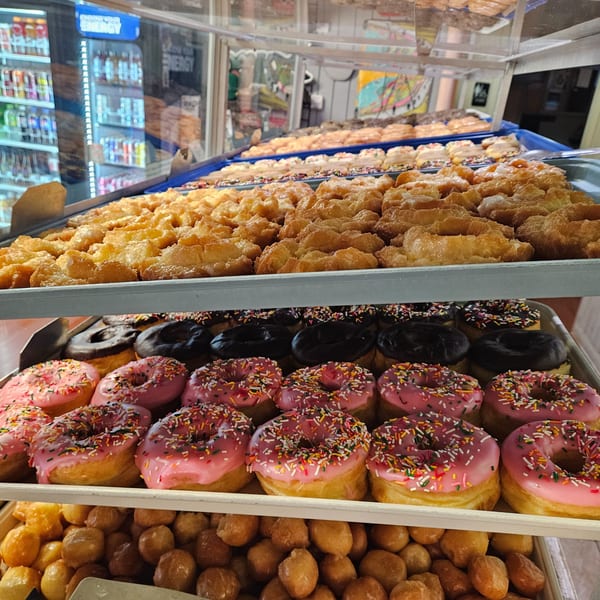 A display case filled with various Dank Donuts, including glazed, chocolate, and pink frosted with sprinkles.