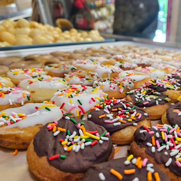A close-up of Dank Donuts' mini donuts, some with white icing and others with chocolate, all covered in colorful sprinkles.