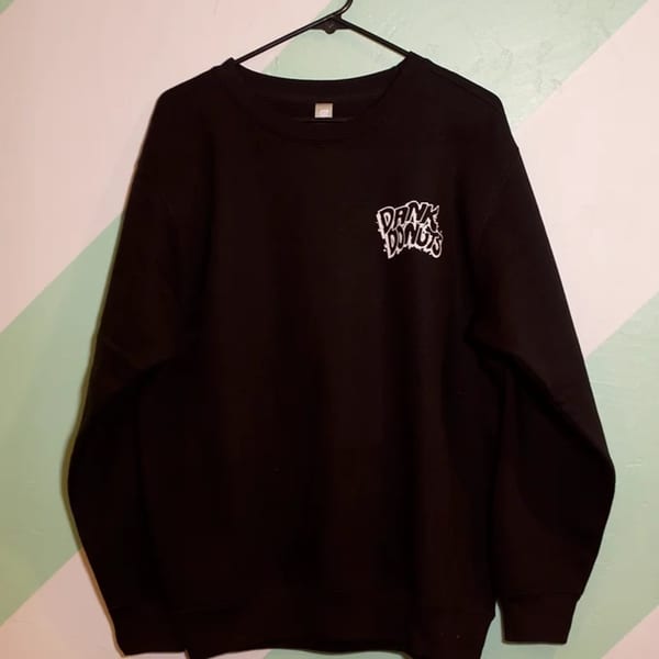 Black Dank Donuts sweatshirt with white logo hanging on a hanger against a two-toned wall.