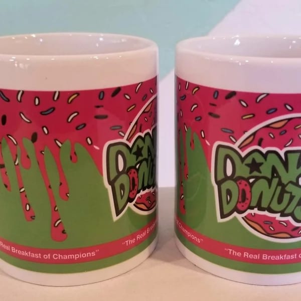 Two Dank Donuts mugs with pink frosting, green drips, sprinkles, and the slogan "The Real Breakfast of Champions".